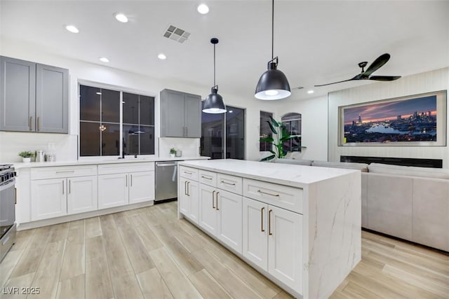 kitchen with light stone counters, ceiling fan, decorative light fixtures, dishwasher, and a kitchen island