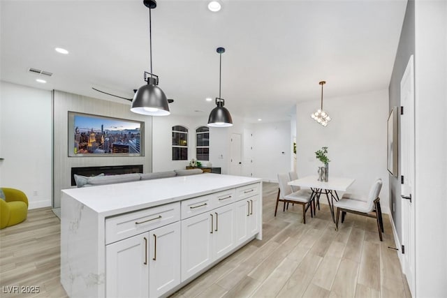 kitchen featuring white cabinets, decorative light fixtures, a center island, and light wood-type flooring