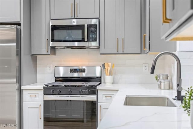 kitchen featuring decorative backsplash, appliances with stainless steel finishes, light stone countertops, gray cabinetry, and sink