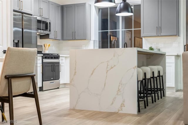 kitchen with light stone countertops, appliances with stainless steel finishes, tasteful backsplash, gray cabinets, and hanging light fixtures