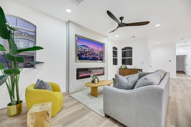 living room with ceiling fan, a fireplace, and light hardwood / wood-style floors