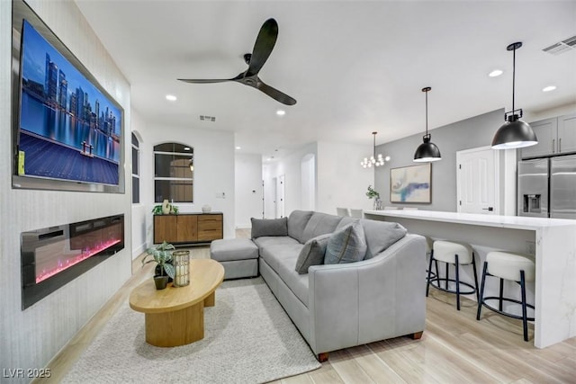 living room featuring ceiling fan with notable chandelier and light hardwood / wood-style floors