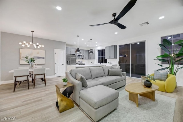 living room featuring ceiling fan with notable chandelier and light hardwood / wood-style flooring