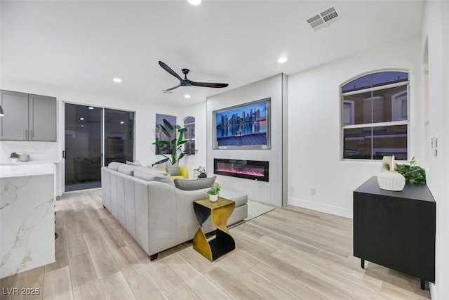 living room featuring ceiling fan, light hardwood / wood-style floors, and a fireplace