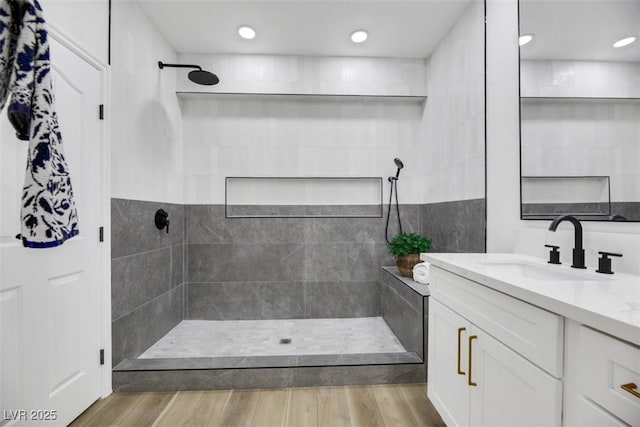 bathroom featuring a tile shower, vanity, and wood-type flooring