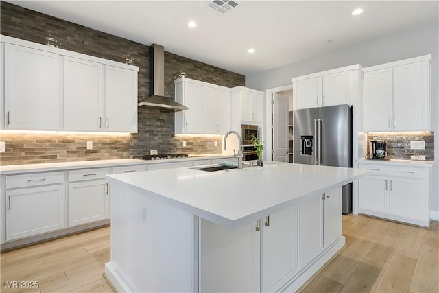 kitchen with white cabinetry, appliances with stainless steel finishes, a center island with sink, and wall chimney exhaust hood