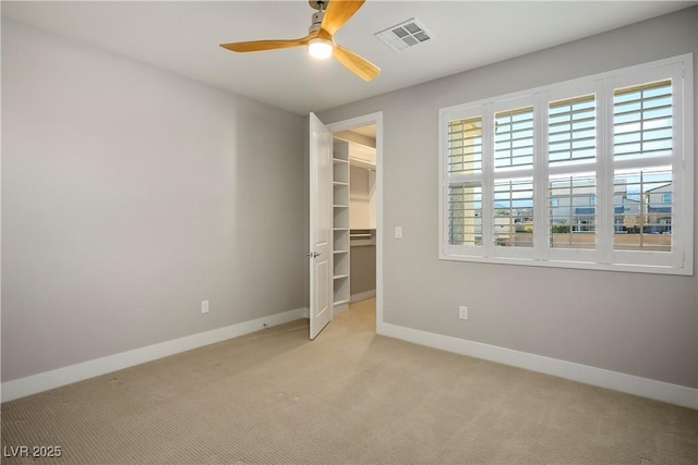 unfurnished bedroom featuring a closet, a walk in closet, light colored carpet, and ceiling fan