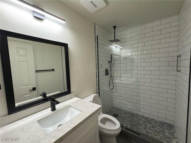 bathroom featuring toilet, vanity, and tiled shower