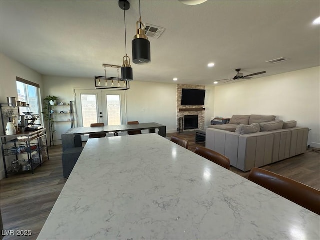 kitchen with dark wood-type flooring, ceiling fan, a fireplace, decorative light fixtures, and a kitchen island