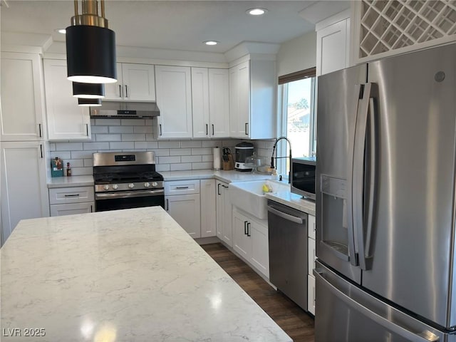 kitchen featuring light stone countertops, white cabinetry, sink, stainless steel appliances, and decorative light fixtures