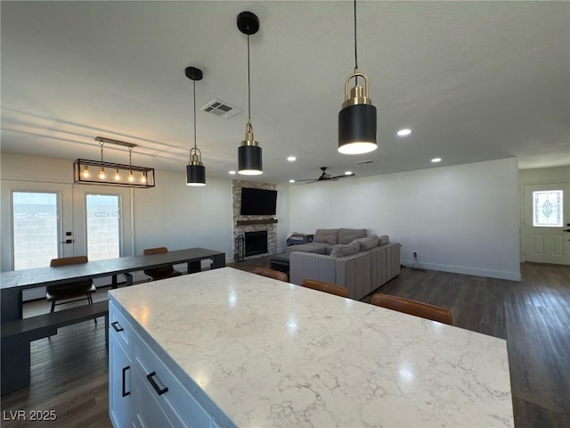 kitchen featuring ceiling fan, dark wood-type flooring, a fireplace, a kitchen island, and hanging light fixtures