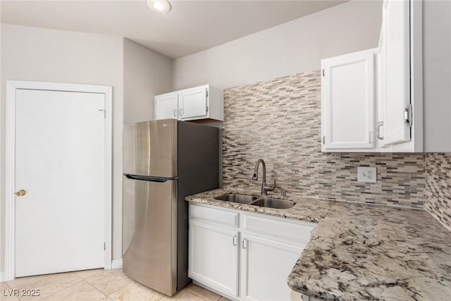 kitchen with sink, white cabinets, light stone countertops, and stainless steel fridge