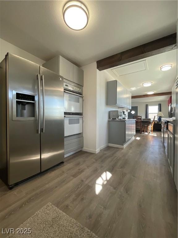 kitchen with white cabinetry, beamed ceiling, hardwood / wood-style floors, stainless steel fridge with ice dispenser, and double oven