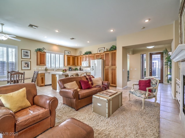 tiled living room featuring ceiling fan, sink, and a fireplace