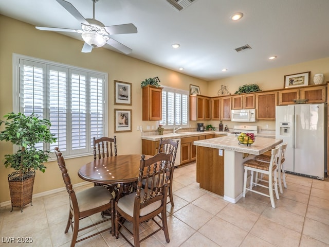 kitchen featuring white appliances, ceiling fan, light tile patterned floors, a breakfast bar area, and a kitchen island