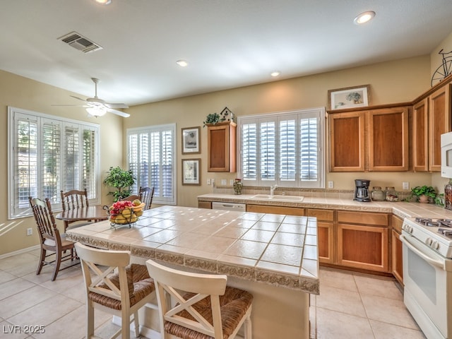 kitchen featuring white appliances, a breakfast bar area, light tile patterned floors, ceiling fan, and sink