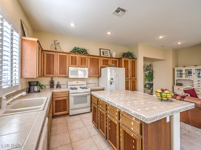 kitchen with sink, tile countertops, white appliances, light tile patterned floors, and a kitchen island