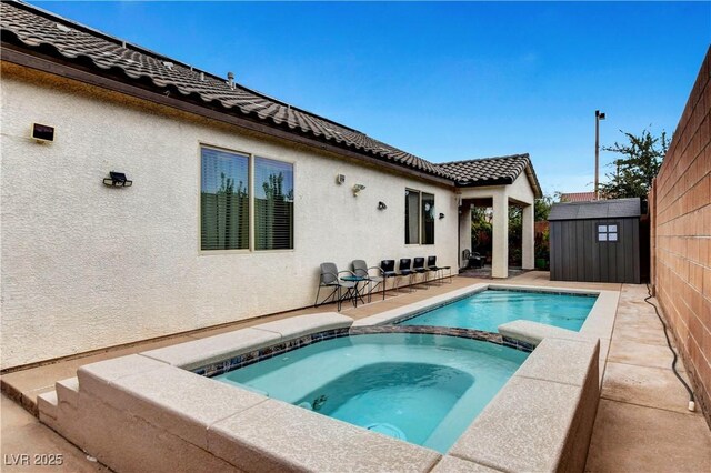 view of swimming pool featuring an in ground hot tub, a storage shed, and a patio