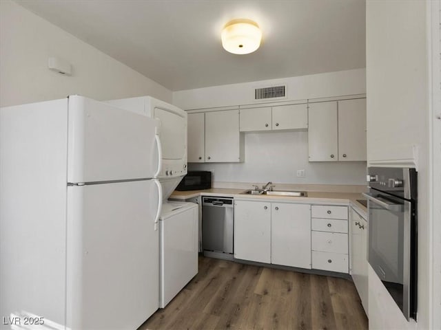 kitchen with dark wood-type flooring, stainless steel appliances, white cabinets, stacked washer and clothes dryer, and sink