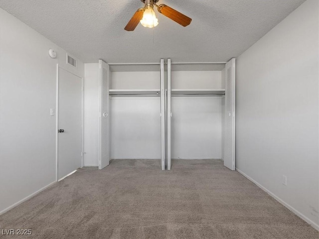 unfurnished bedroom with ceiling fan, two closets, light carpet, and a textured ceiling