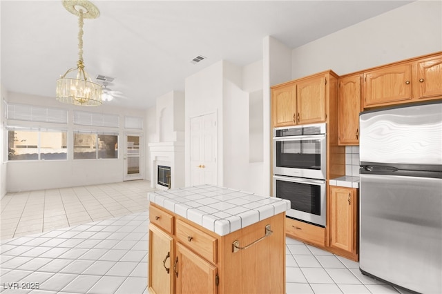 kitchen featuring tile counters, appliances with stainless steel finishes, a kitchen island, decorative light fixtures, and light tile patterned flooring