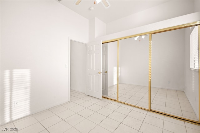 unfurnished bedroom with a towering ceiling, light tile patterned flooring, a closet, and ceiling fan