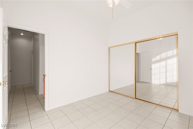 unfurnished bedroom with a towering ceiling, ceiling fan, a closet, and light tile patterned floors