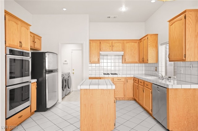 kitchen featuring a center island, tile countertops, backsplash, washer and dryer, and appliances with stainless steel finishes