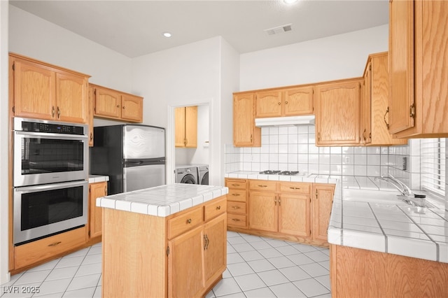 kitchen featuring tile counters, a kitchen island, separate washer and dryer, appliances with stainless steel finishes, and light tile patterned flooring