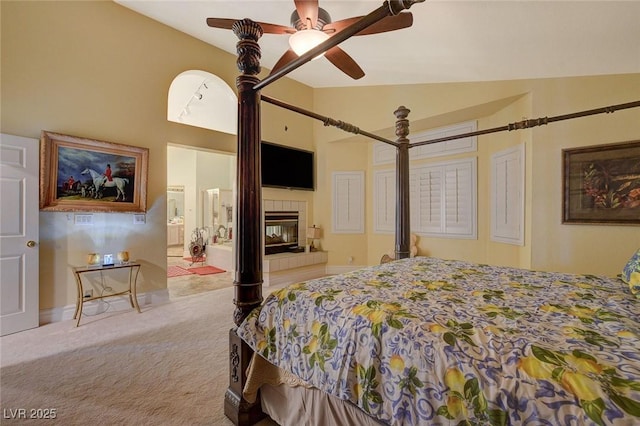 carpeted bedroom featuring ensuite bathroom, a tiled fireplace, high vaulted ceiling, and ceiling fan