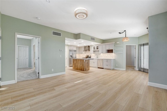 kitchen featuring stainless steel appliances, white cabinetry, tasteful backsplash, a kitchen island, and wall chimney range hood