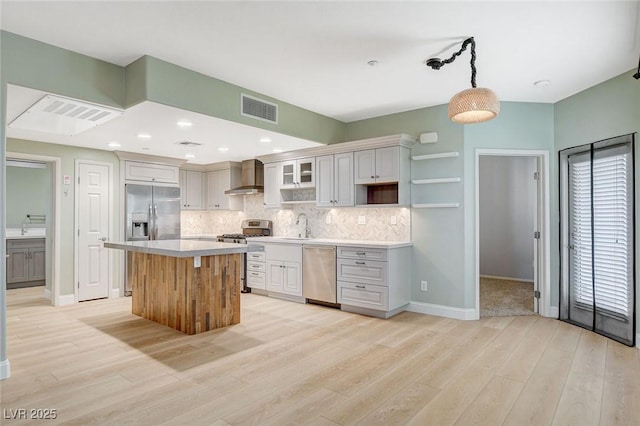 kitchen with wall chimney exhaust hood, hanging light fixtures, stainless steel appliances, a kitchen island, and backsplash