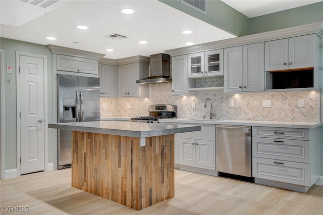 kitchen with stainless steel appliances, a center island, wall chimney exhaust hood, sink, and light hardwood / wood-style flooring