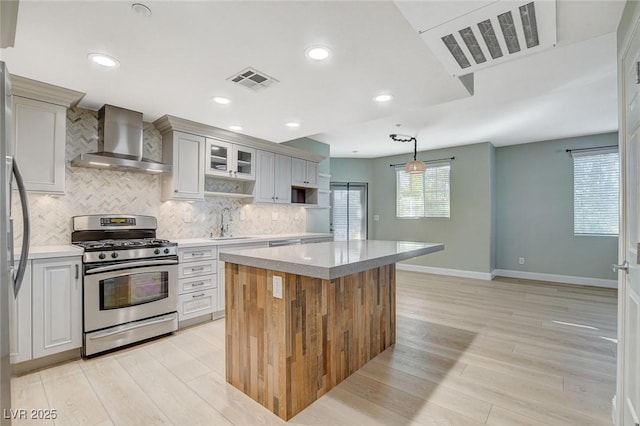 kitchen featuring wall chimney exhaust hood, pendant lighting, a kitchen island, stainless steel range with gas stovetop, and sink