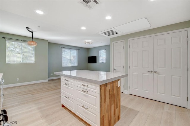 kitchen with white cabinets, light wood-type flooring, light stone countertops, a kitchen island, and pendant lighting