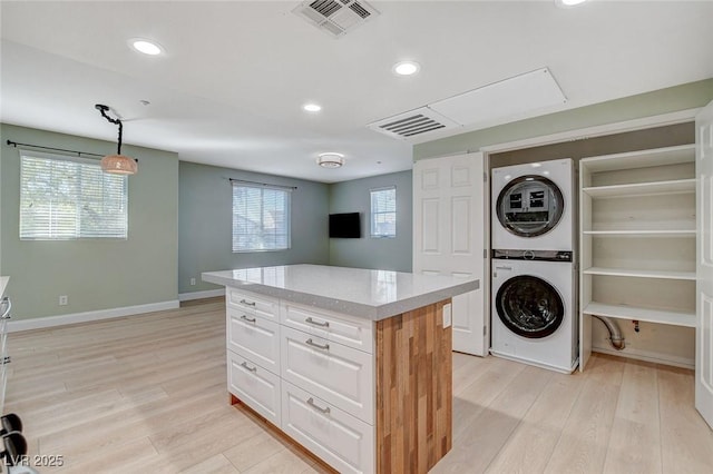 kitchen featuring stacked washer / dryer, a center island, pendant lighting, a wealth of natural light, and white cabinets