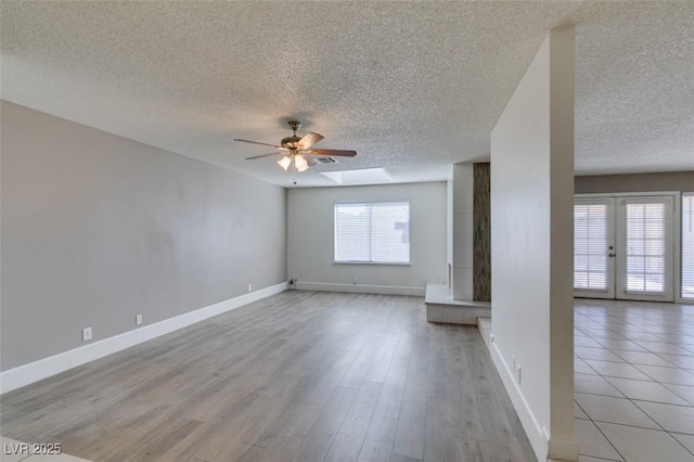 unfurnished living room featuring a textured ceiling, french doors, ceiling fan, light hardwood / wood-style flooring, and a skylight