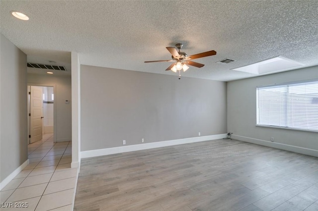 spare room with ceiling fan, a skylight, a textured ceiling, and light hardwood / wood-style floors