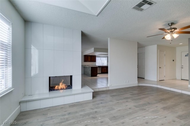 unfurnished living room with a textured ceiling, a fireplace, ceiling fan, and light hardwood / wood-style floors