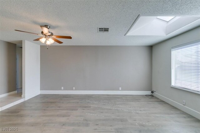 spare room featuring ceiling fan, light hardwood / wood-style flooring, a skylight, and a textured ceiling