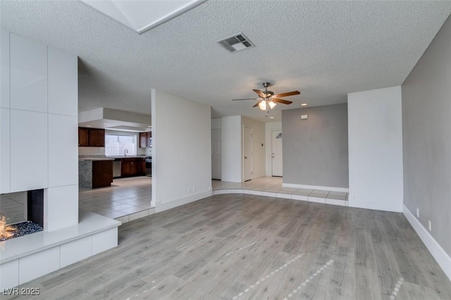 unfurnished living room with a tile fireplace, light hardwood / wood-style floors, ceiling fan, a textured ceiling, and sink