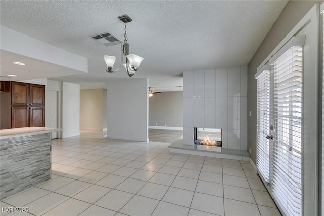 unfurnished living room featuring a textured ceiling, a multi sided fireplace, ceiling fan with notable chandelier, and light tile patterned floors