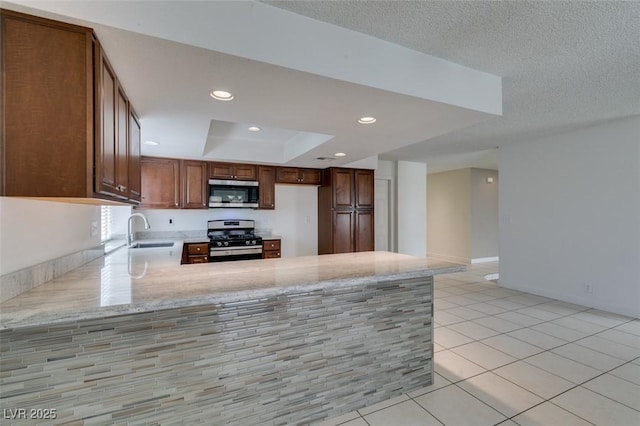 kitchen featuring appliances with stainless steel finishes, kitchen peninsula, light tile patterned floors, a tray ceiling, and sink