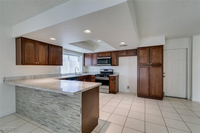 kitchen featuring kitchen peninsula, a raised ceiling, light tile patterned floors, appliances with stainless steel finishes, and sink