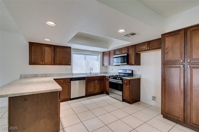 kitchen featuring sink, light tile patterned floors, kitchen peninsula, a tray ceiling, and appliances with stainless steel finishes