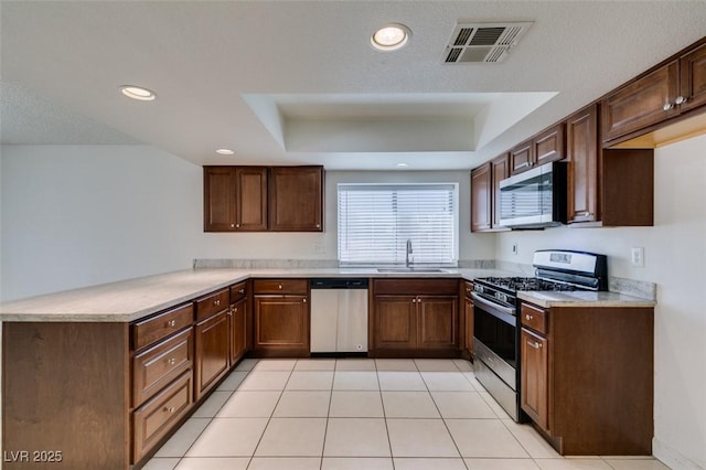 kitchen with light tile patterned flooring, appliances with stainless steel finishes, a tray ceiling, and sink