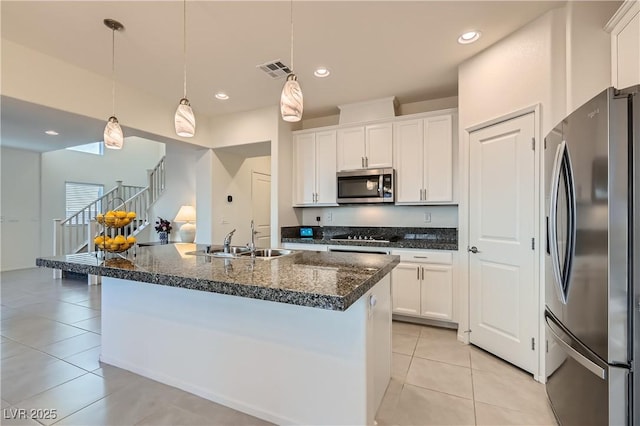 kitchen with stainless steel appliances, an island with sink, sink, white cabinetry, and decorative light fixtures