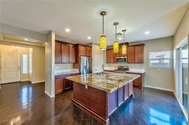 kitchen featuring light stone countertops, decorative light fixtures, stainless steel appliances, an island with sink, and sink