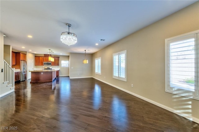 unfurnished living room featuring a notable chandelier, dark hardwood / wood-style flooring, and plenty of natural light