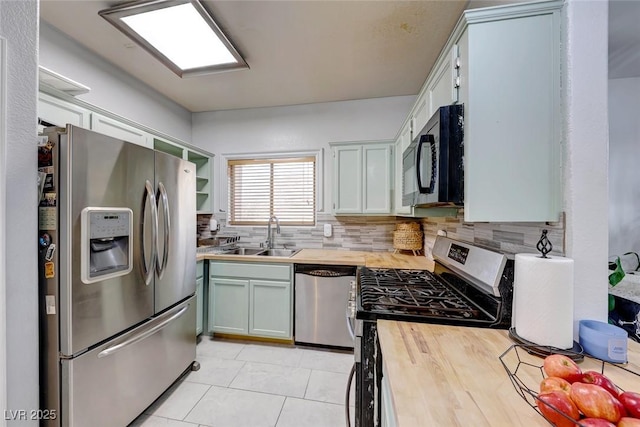 kitchen featuring stainless steel appliances, wood counters, decorative backsplash, sink, and light tile patterned flooring